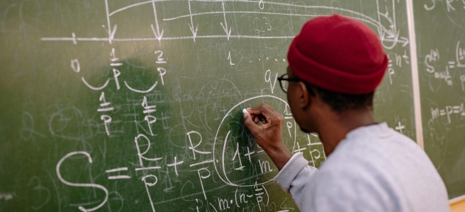 A man writes equations on a blackboard