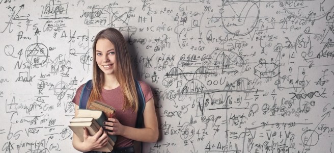 A female student stands in front of a whiteboard covered with complex text and equations